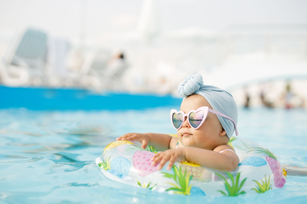 a young baby floating in a pool with sunglasses and headwrap